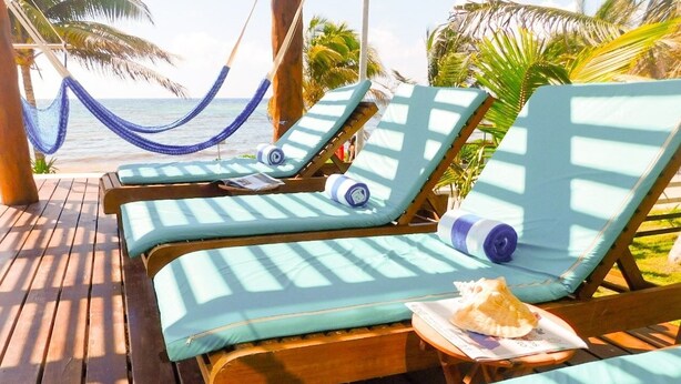 A wooden deck with lounge chairs and a hammock, overlooking a beach with palm trees. - Aquastar By RT Vacation Rentals (Mahahual)