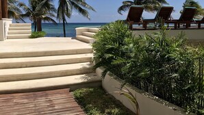 A wooden deck leading to a pool area with lounge chairs and palm trees. - Aquastar By RT Vacation Rentals (Mahahual)