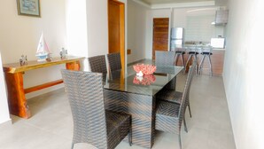 A dining area with a glass-top table, wicker chairs, a wooden bench, and a small decorative sailboat model. - Aquastar By RT Vacation Rentals (Mahahual)