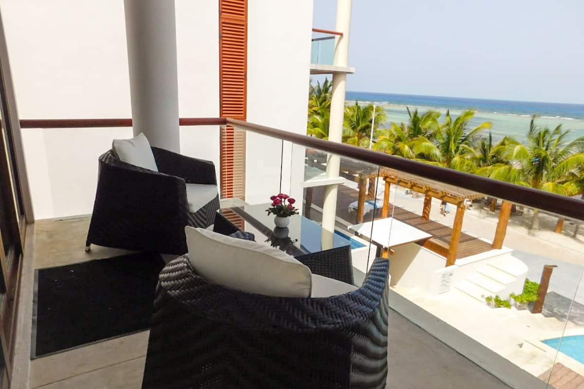 A balcony with a view of the ocean, a glass table, and two black wicker chairs with cushions.
