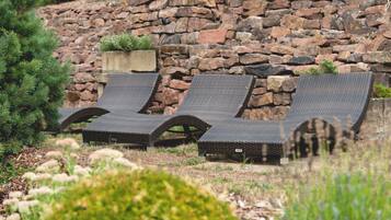 Tres cadires de vimar amb estructura metàl·lica, col·locades davant d'una paret de pedra amb una petita jardiniera.