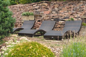 Tres sillas de mimbre con estructura de metal, ubicadas frente a un muro de piedra con una maceta pequeña.