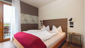 A modern hotel room with a large bed, a red throw blanket, a small table with fruit, and a view of the outdoors.