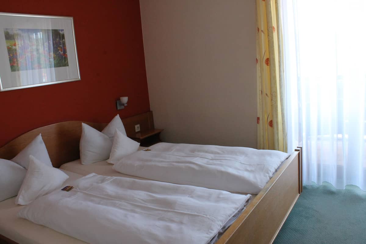 A double bed with white bedding in a room with red walls and a framed picture on the wall.