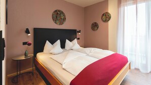 A hotel room with a large bed, a bedside table with a vase, and decorative wall art. - Hotel Restaurant Martha (Wertheim)