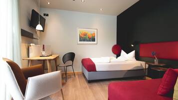 A hotel room with a bed, a desk, a chair, a TV, and a painting on the wall.