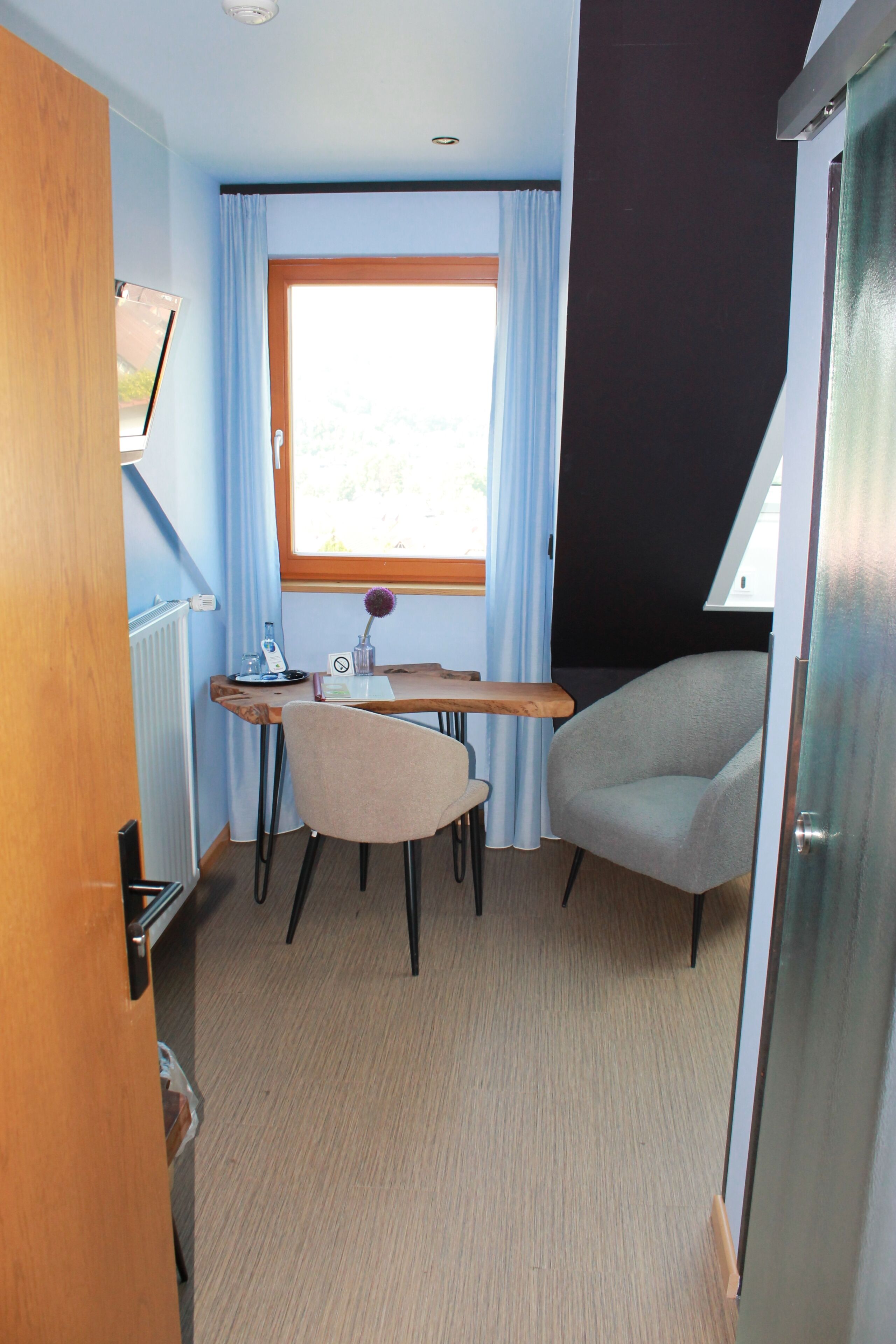 A compact room with a desk, two chairs, a radiator, and a window with curtains.