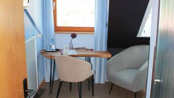 A compact room with a desk, two chairs, a radiator, and a window with curtains.