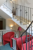 Una escalera con barandillas negras, una silla roja y una mesita con una lámpara.