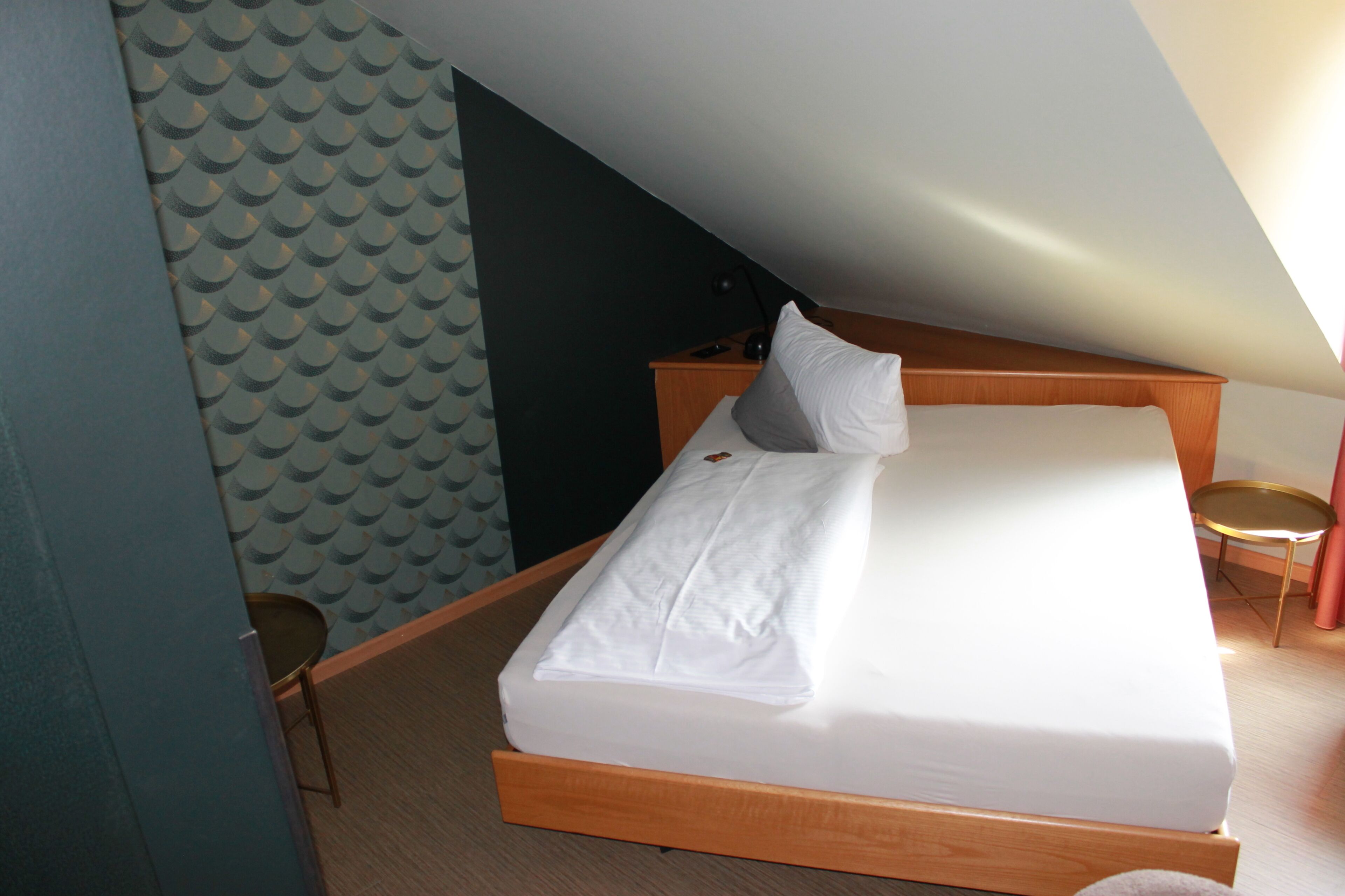 Una cama individual con estructura de madera y ropa de cama blanca en una habitación con techo inclinado.