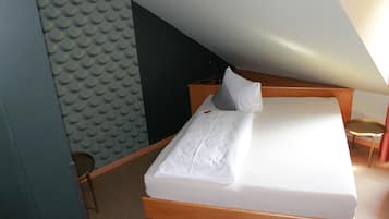 Una cama individual con estructura de madera y ropa de cama blanca en una habitación con techo inclinado.