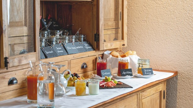 Um buffet de café da manhã com diversas opções de comida e bebida, incluindo frutas, queijos e mel.