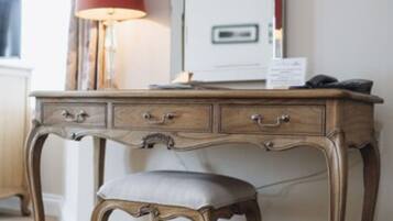 A wooden desk with drawers and a cushioned bench, a red lamp, and a mirror on the wall.