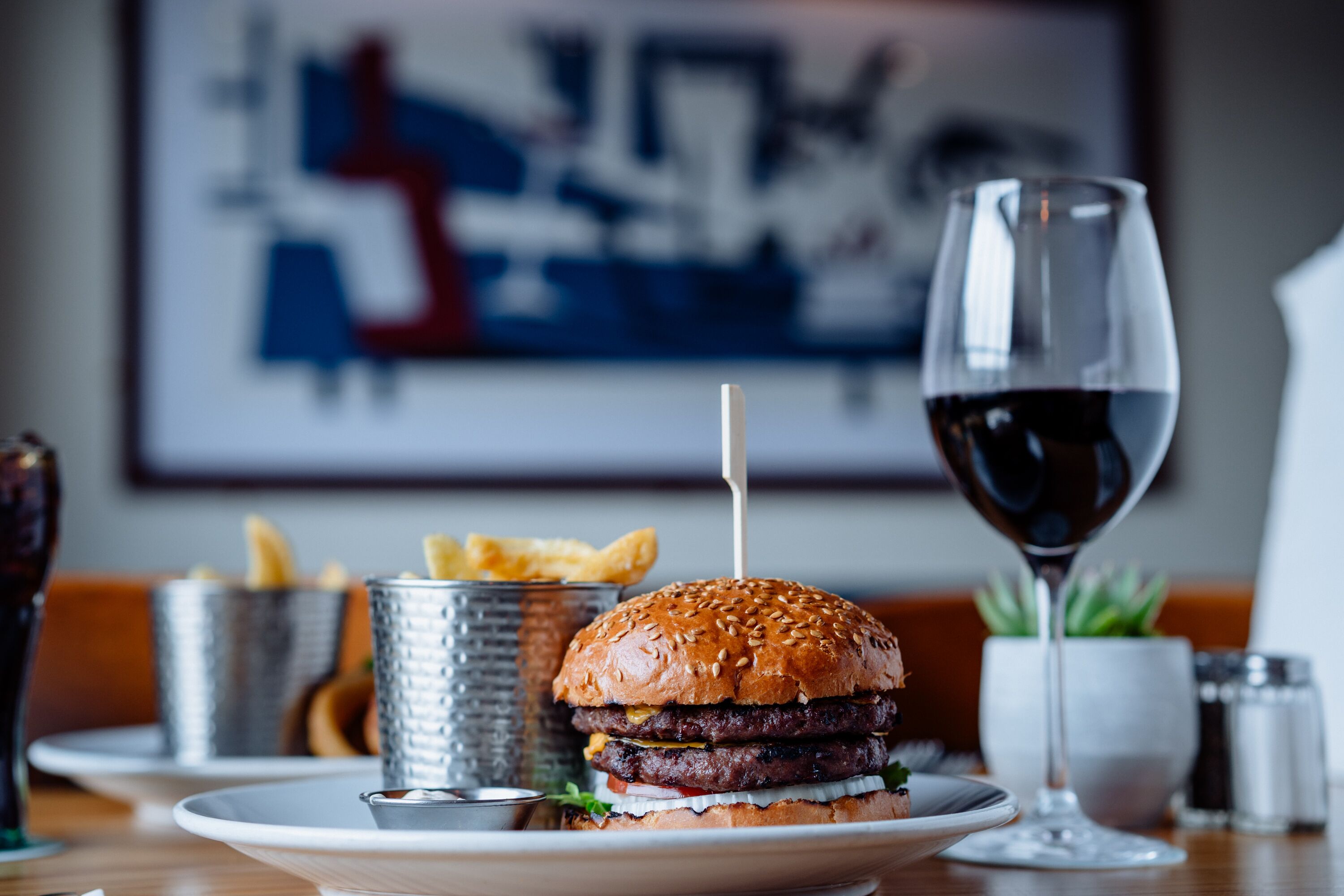 Hambúrguer com batatas fritas e um copo de vinho tinto sobre uma mesa.