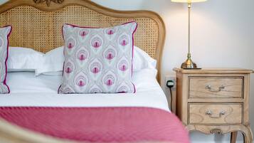 A neatly made bed with a white and pink patterned pillow, a wooden nightstand with drawers, and a bedside lamp.