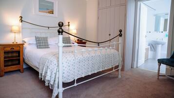 A neatly arranged bedroom with a bed, bedside tables, a chair, and a door leading to a bathroom.