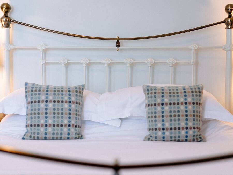 A neatly made bed with white bedding and two patterned pillows, a white headboard, and a brass rod across the top.