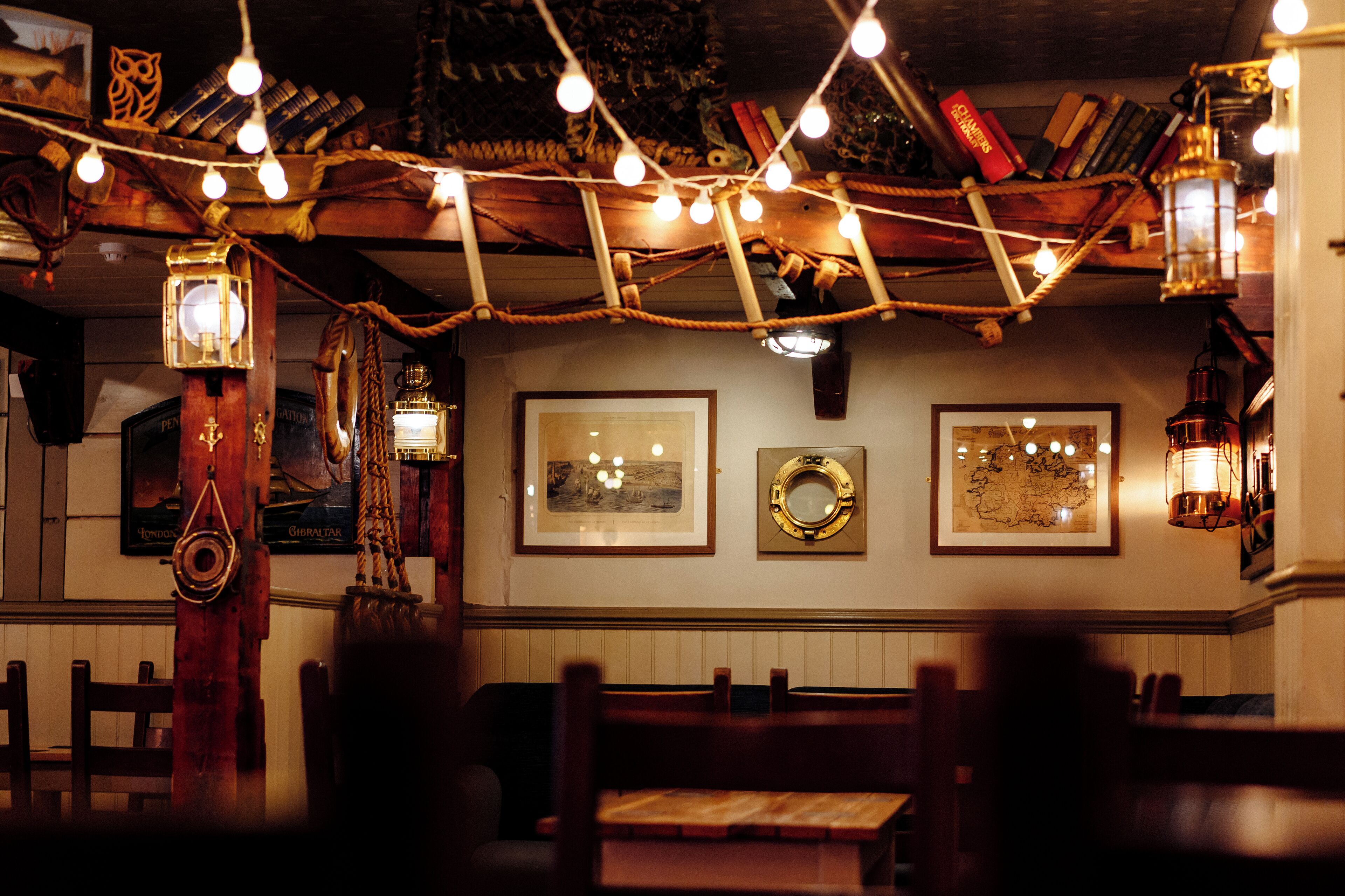 Un restaurant à l’ambiance chaleureuse, avec des meubles en bois, des guirlandes lumineuses et une décoration sur le thème de la mer.