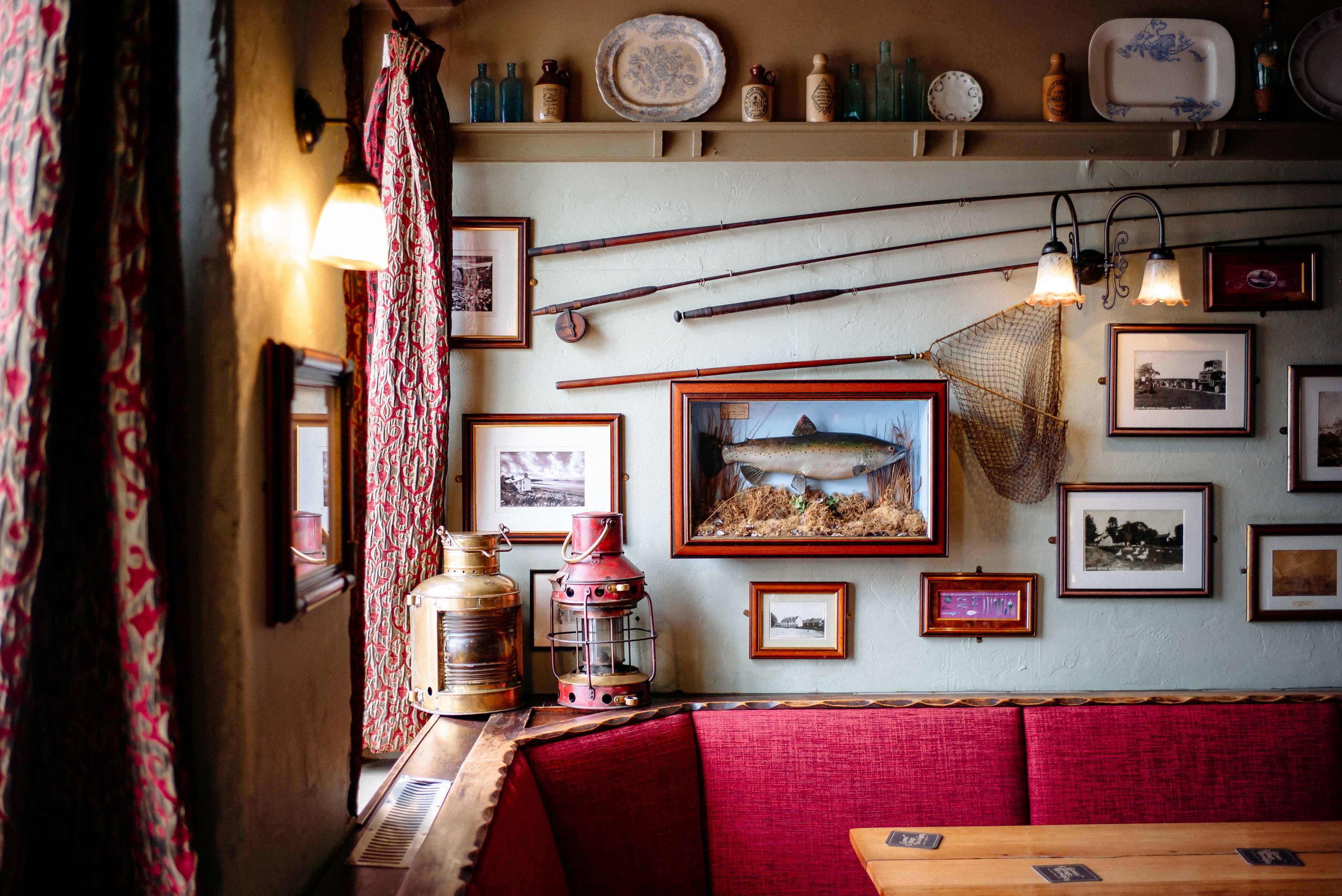Een restaurantinterieur met rode, beklede zittingen, ingelijste foto's aan de muur en verschillende flessen op planken.