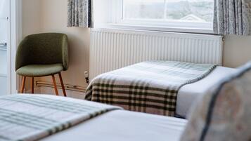 A bedroom with two beds, a chair, a radiator, and a window with curtains.