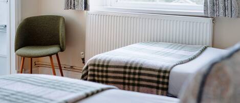A bedroom with two beds, a chair, a radiator, and a window with curtains.