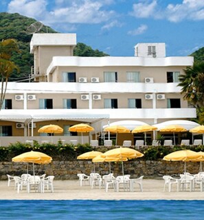 A hotel with multiple floors, outdoor seating with yellow umbrellas, and a pool area. - Hotel Torremolinos (Ubatuba)