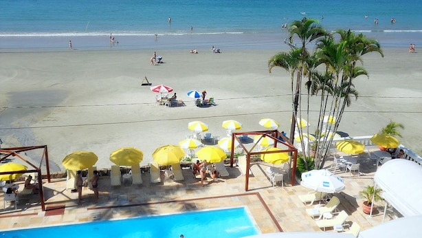 Un complejo turístico en la playa con piscina, tumbonas y sombrillas.