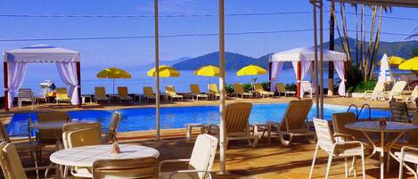 A poolside area with lounge chairs, umbrellas, and a view of the sea.