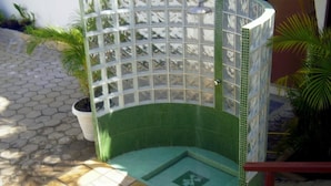 Un área de ducha exterior pequeña y cerrada, con piso de azulejos y baranda de metal.