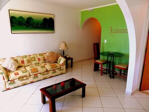A living room with a sofa, a coffee table, a lamp, and a dining area with a table and chairs. - Hotel Torremolinos (Ubatuba)