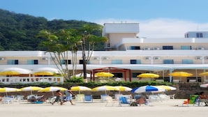 Un hotel con varios pisos, mobiliario exterior con sombrillas y vista al mar.