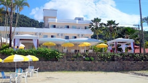 Un hotel frente a la playa con varios sombrillas amarillas, sillas blancas y un muro de piedra.