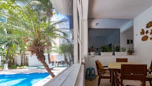Ein Balkon mit Blick auf einen Swimmingpool, Holzstühle, ein Tisch und Kübelpflanzen.
