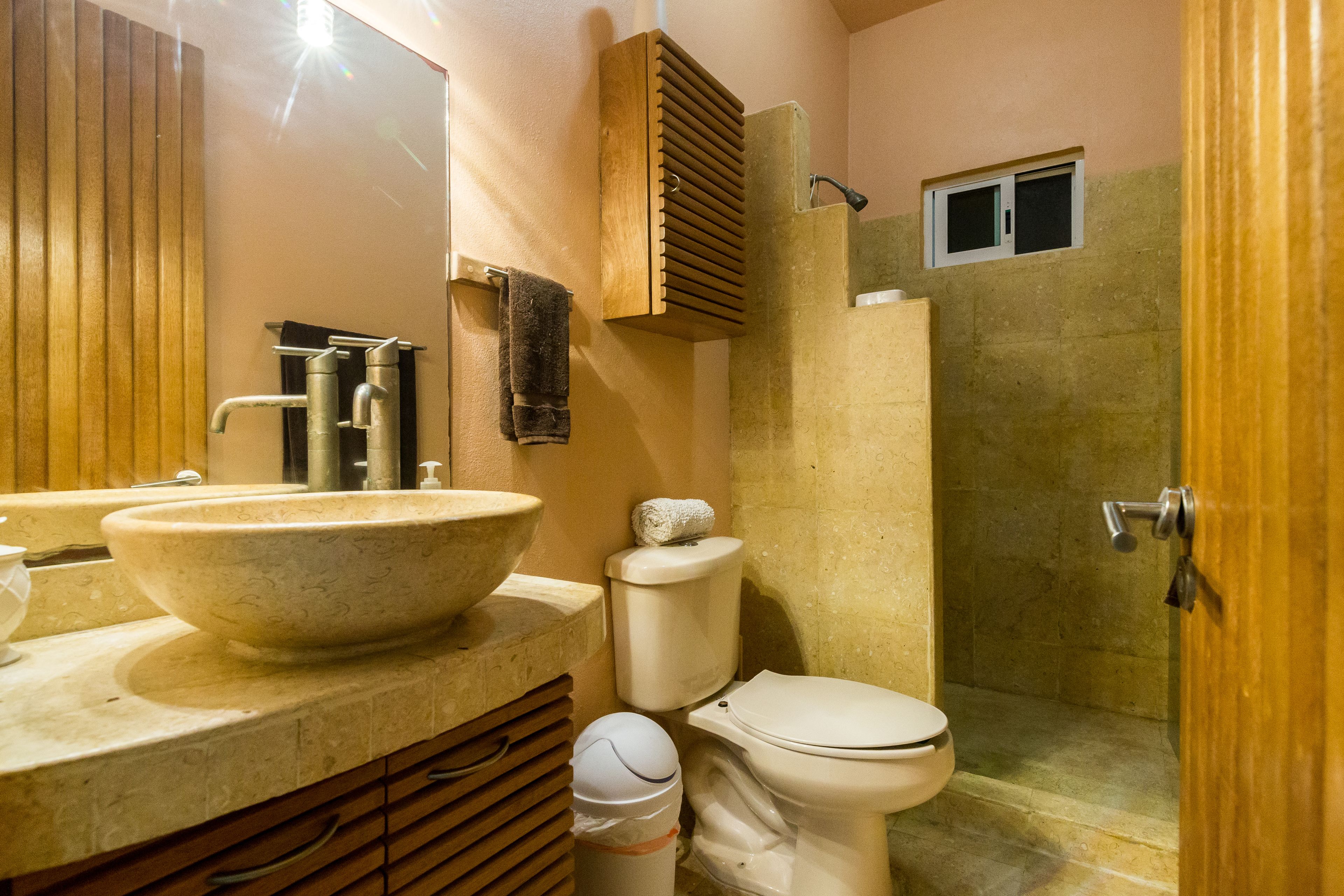 A bathroom with a large vessel sink, a toilet, a shower enclosure, and a wooden vanity.