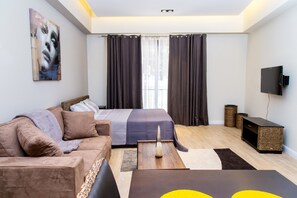 A modern bedroom with a bed, a sofa, a TV, and a flat-screen TV mounted on the wall. - PLS Apartments - Cantonments (Accra)