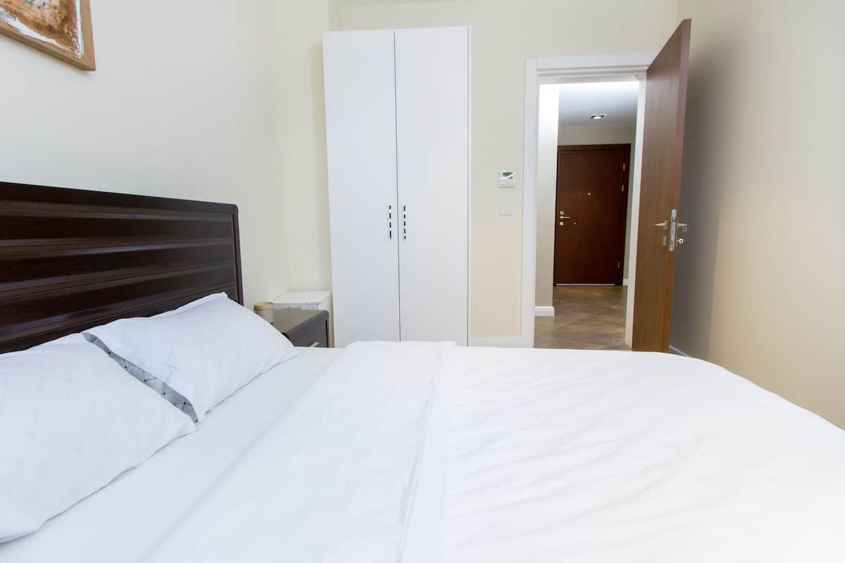 A hotel room with a large bed, a wardrobe, a nightstand, and a door leading to another room.