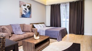 A modern bedroom with a bed, a sofa, a coffee table, and a painting on the wall. - PLS Apartments - Cantonments (Accra)