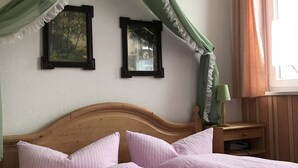 Een slaapkamer met een houten hoofdbord, twee roze kussens, een groen hemelbed en twee ingelijste foto's aan de muur.