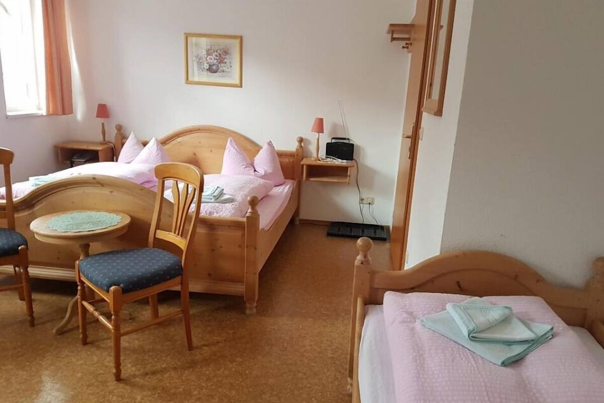 Een slaapkamer met een houten bed, een klein rond tafeltje, twee stoelen, een nachtkastje met een lamp en een aan de muur bevestigde televisie.