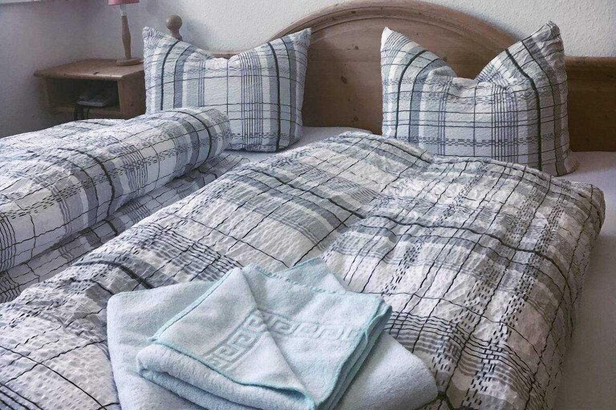 Een netjes opgemaakt bed met een geborreld sprei en kussens, een nachtkastje met een lamp, en een ingelijst schilderij aan de muur.