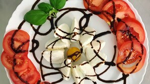 Een bord Caprese salade met tomaten, mozzarella en basilicum, overgoten met balsamico glazuur.