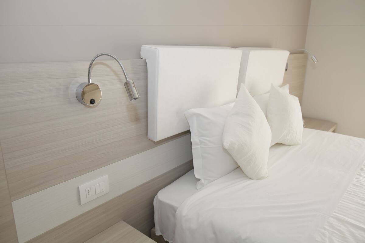 Een moderne hotelkamer met een netjes opgemaakt bed, een bedieningspaneel aan de muur en een stopcontact.