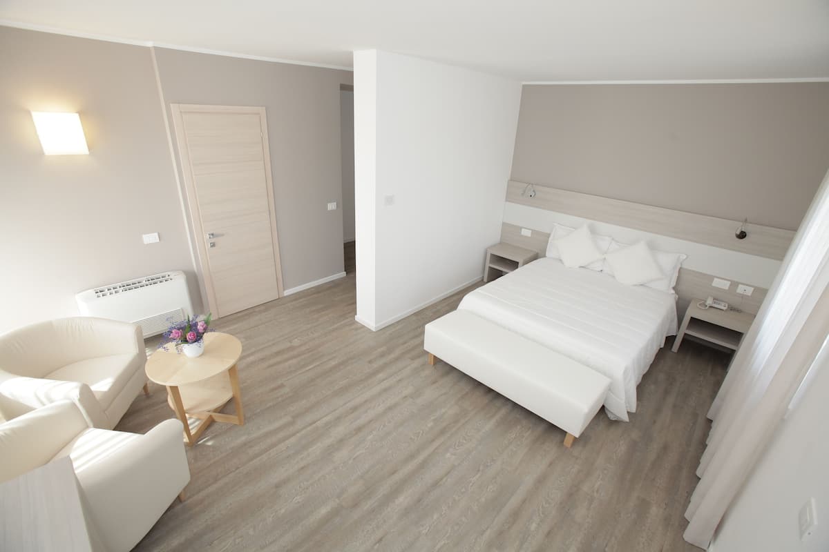 Een hotelkamer met een bed, een stoel, een klein tafeltje met bloemen en een nachtkastje met een lamp.