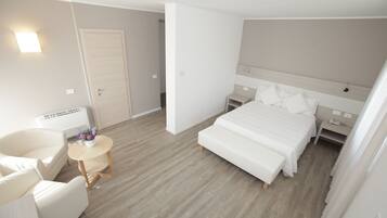 Una camera d'albergo con un letto, una sedia, un tavolino con fiori e un comodino con una lampada.