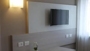 A modern hotel room with a flat-screen TV mounted on a wall, a wooden desk with a small vase, and a window with curtains. - Hotel Europa (Marostica)