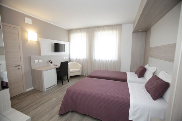 Una habitación de hotel con dos camas, un escritorio, una silla y un televisor.