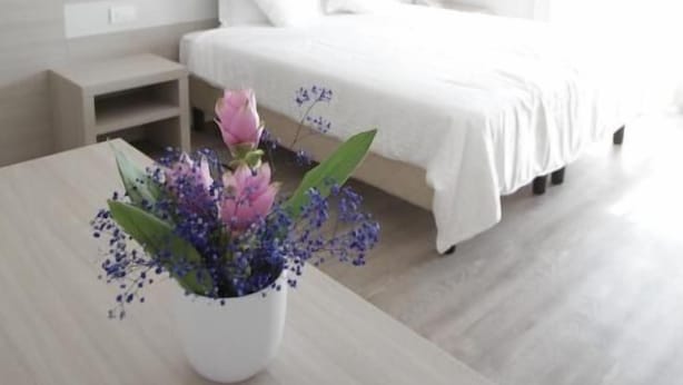 A modern hotel room with a bed, bedside tables, a nightstand, and a vase with flowers on a wooden table. - Hotel Europa (Marostica)