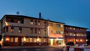 Un hotel a più piani con ingresso a livello strada, numerose finestre su ogni piano e un'antenna parabolica sul tetto.