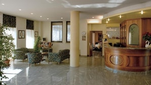 A spacious lobby with a reception desk, seating area with patterned chairs, and a large pillar. - Hotel Europa (Marostica)