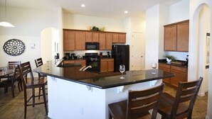 A modern kitchen with wooden cabinets, a central island, and a dining area with chairs.